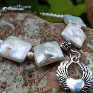 bracelet souple en perles biwa sur fil cablé, fermoir en T. Breloque charme coeur ailé.
